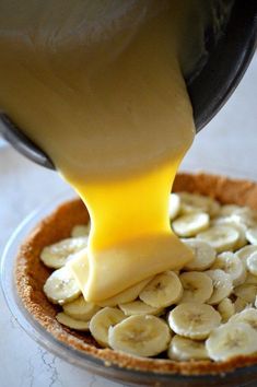 someone is pouring cheese on top of banana slices in a pie crust with other toppings