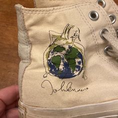 someone is holding up a pair of shoes with the earth painted on them