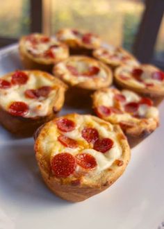 mini pepperoni pizzas on a white plate next to a cupcake tin and window