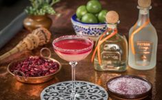 a pink cocktail in a coupe glass on top of a table next to bottles of alcohol