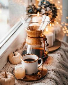 a cup of coffee on a tray next to a window sill with candles and pumpkins