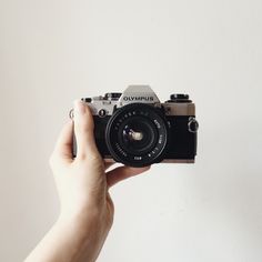 a person holding up a camera in front of a white wall