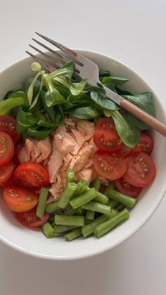 a white bowl filled with green beans, tomatoes and sliced meat next to a fork