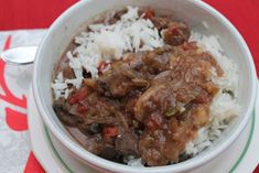 a white bowl filled with rice and meat on top of a red table cloth next to a spoon