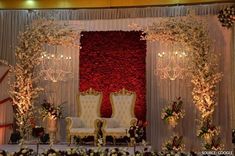 a stage set up for a wedding with chairs and flowers on the wall, surrounded by candles