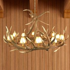 a chandelier made out of antlers hanging from a wooden ceiling with lights on it