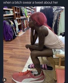 a woman with pink hair is sitting on the floor in front of a rack of clothes