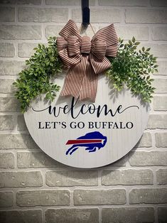 a sign that says welcome let's go buffalo hanging on a brick wall with a bow