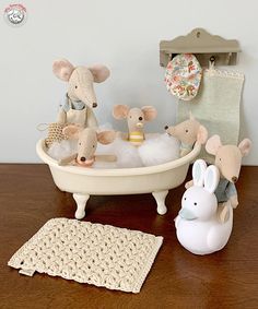 several stuffed animals are sitting in a bathtub on a table next to a crocheted rug