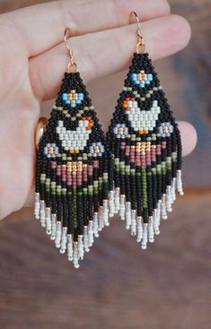 a pair of black and white beaded earrings with birds on them, hanging from gold - plated hooks