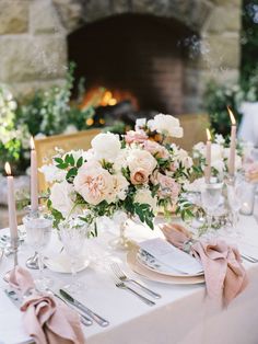 the table is set with white and pink flowers, silverware, candles and napkins