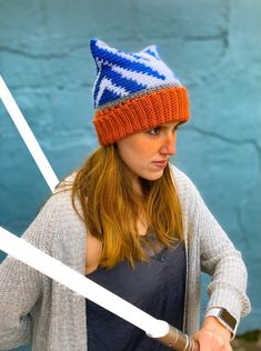 a woman wearing a knitted hat and holding two white swords in front of a blue wall