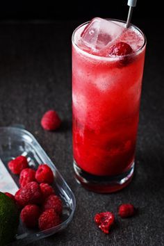 a red drink with ice and raspberries next to it