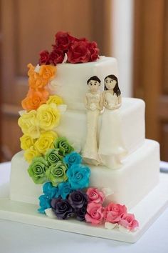 a wedding cake with rainbow roses on the bottom and bride and groom figurines on top