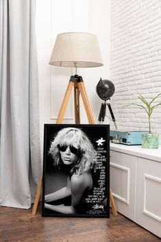 a black and white photo of a blond woman on a easel next to a lamp