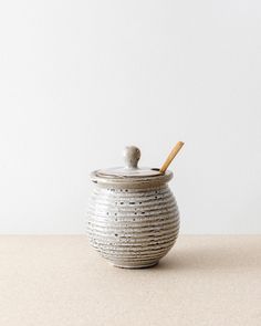 a ceramic jar with a wooden spoon in it on a countertop next to a white wall