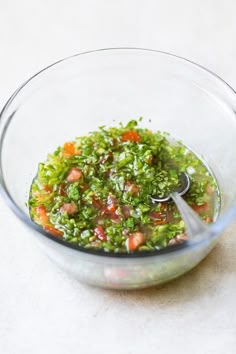 a glass bowl filled with chopped vegetables on top of a white countertop next to a spoon