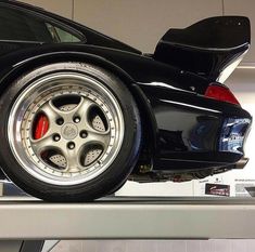 a black sports car parked on top of a metal shelf in a garage with other cars behind it