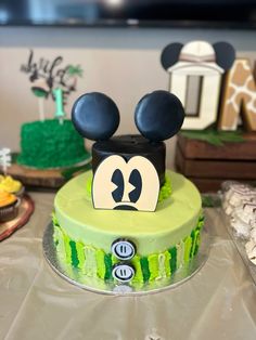 a mickey mouse cake with green frosting and ears on it's head is sitting on a table