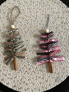 two small christmas trees are sitting on a round tablecloth covered placemat, one is decorated with ribbon and the other has an ornament