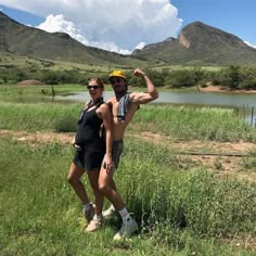 a man and woman posing in front of a body of water with mountains in the background