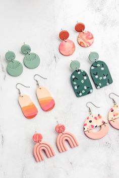 six pairs of colorful earrings on a marble surface with white and green accents, including one in the shape of a cactus