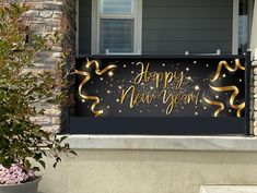 a happy new year banner hanging on the side of a house with flowers in front