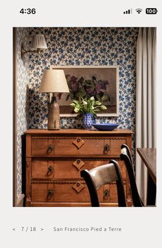 an old dresser with flowers on it and a lamp next to it in the corner