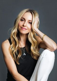 a beautiful blonde woman sitting on top of a chair with her hands behind her head