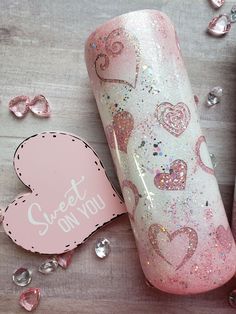 a pink and white bottle with hearts on it next to some confetti pieces