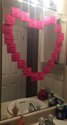 a mirror with pink sticky notes attached to it in front of a white bathroom sink