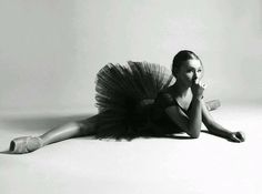 a black and white photo of a woman in ballet attire laying on the floor with her legs crossed