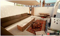 an outdoor living area with couches, tables and rugs on the floor in front of a white wall