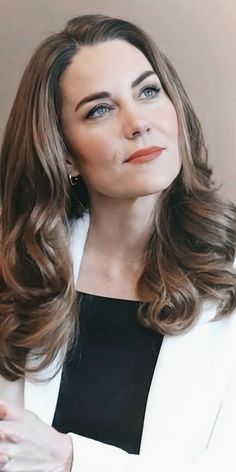 a woman with long brown hair wearing a white blazer and black top smiling at the camera