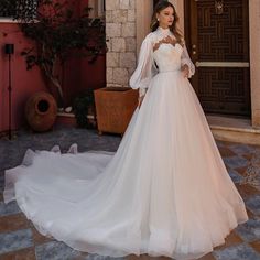 a woman standing in front of a door wearing a wedding dress with long sleeves and an open back