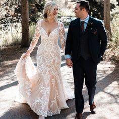 a bride and groom are walking through the woods holding each other's hands as they smile