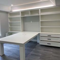 an empty white desk in a room with built - in bookcases and drawers