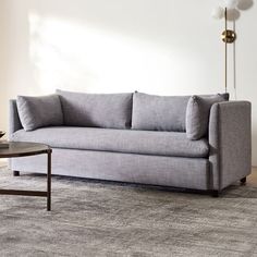 a gray couch sitting on top of a rug in a living room next to a table