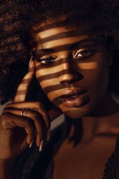 a woman with an afro is posing for the camera and has her hand on her face