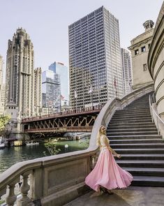 a woman in a pink dress is standing on some steps near the water and buildings