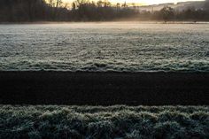 the sun is setting over a frosty field