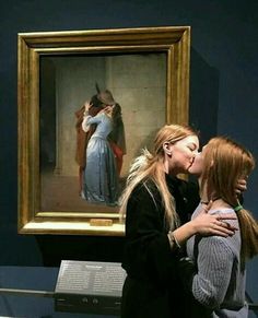 two women standing next to each other in front of a painting on display at a museum