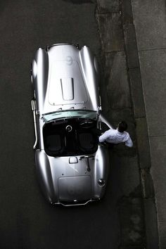 an overhead view of a silver sports car parked on the side of the road with a man standing next to it