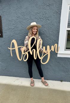 a woman standing in front of a blue wall holding up a wooden sign that says alby