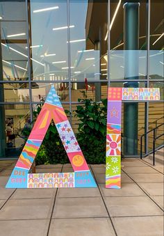 a colorful letter sitting on top of a tiled floor next to a plant in front of a building