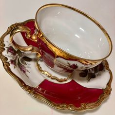 two fancy cups and saucers with gold trimmings on red, white and gold plates