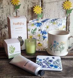 a table topped with a cup, candle and other items next to a box filled with flowers