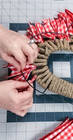 two hands are making a rope wreath with red and white plaid ribbon on the table