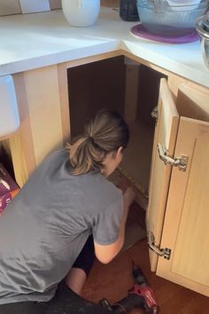 a woman kneeling down in front of a cabinet with tools on the floor next to her