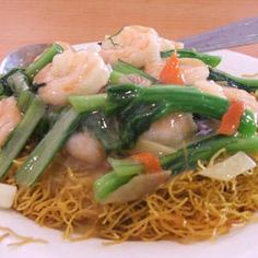 a white plate topped with shrimp and veggies on top of noodles next to a fork